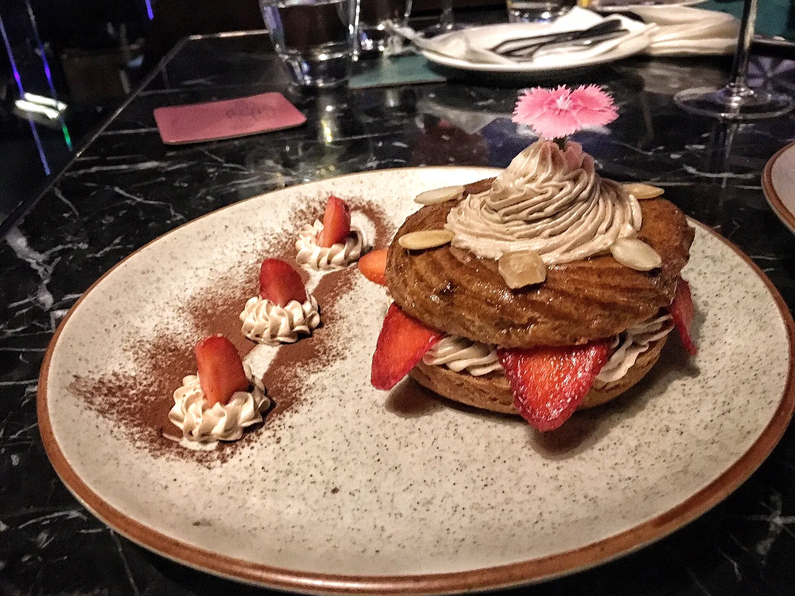 A Paris-Brest style dessert piped with praline cream and strawberries, dusted with cocoa on a speckled ceramic plate.
