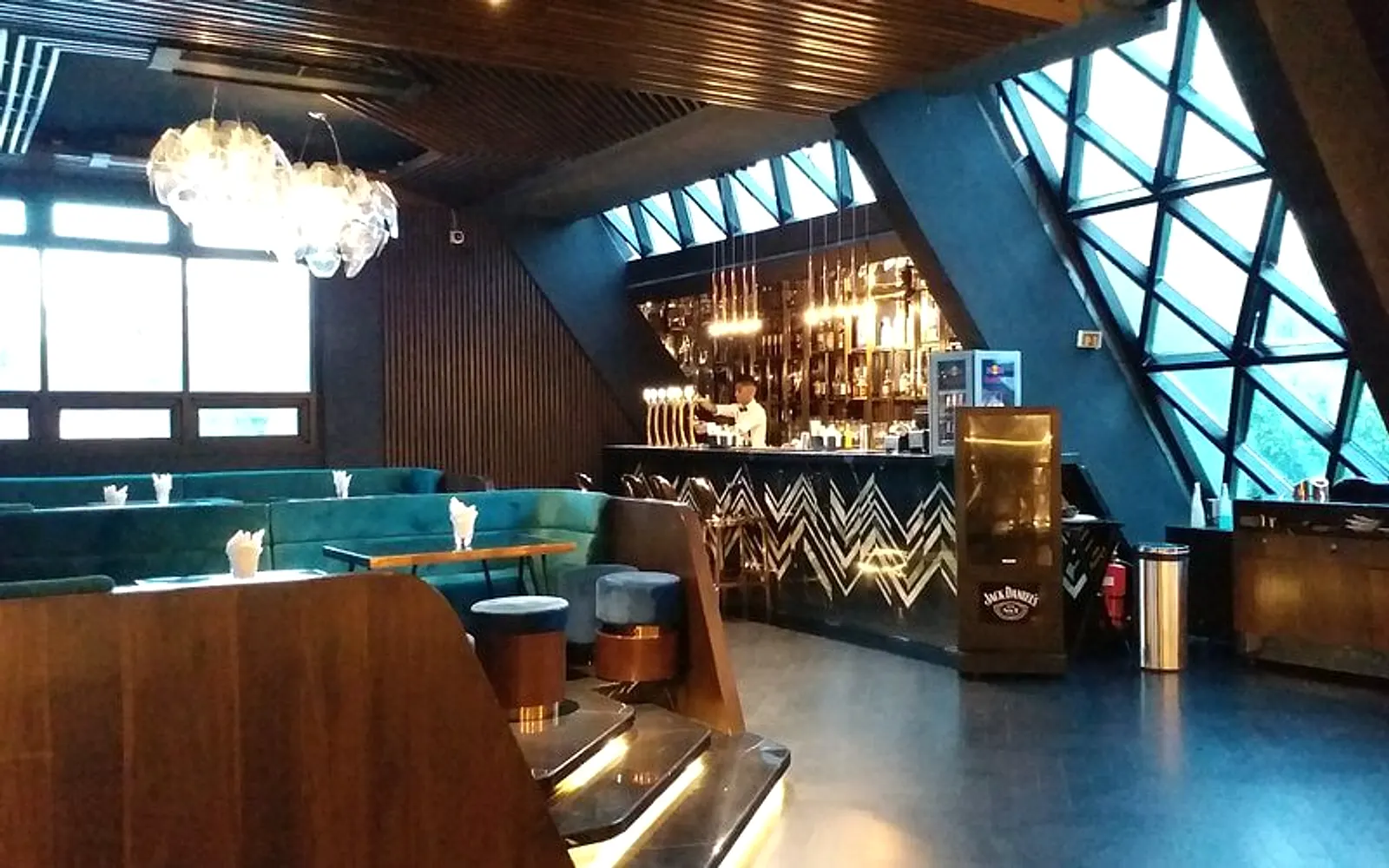 Arena's lounge seating — teal velvet banquettes and brass-footed stools under a slatted wood ceiling and a sculptural glass chandelier.